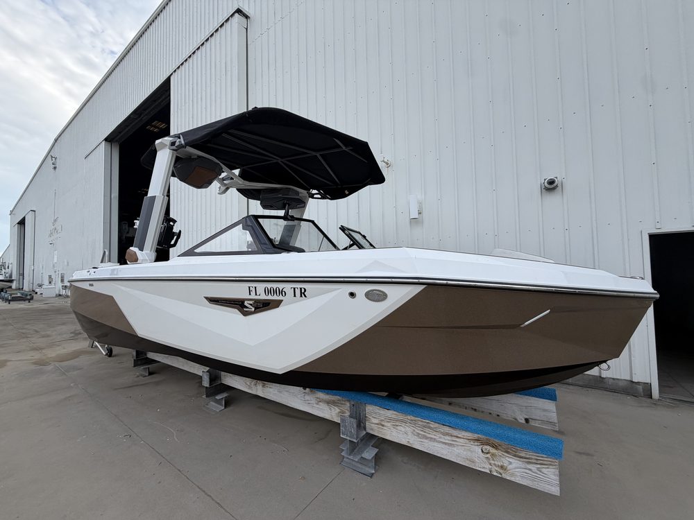 A bronze and white wake boat on stands outside a marina building