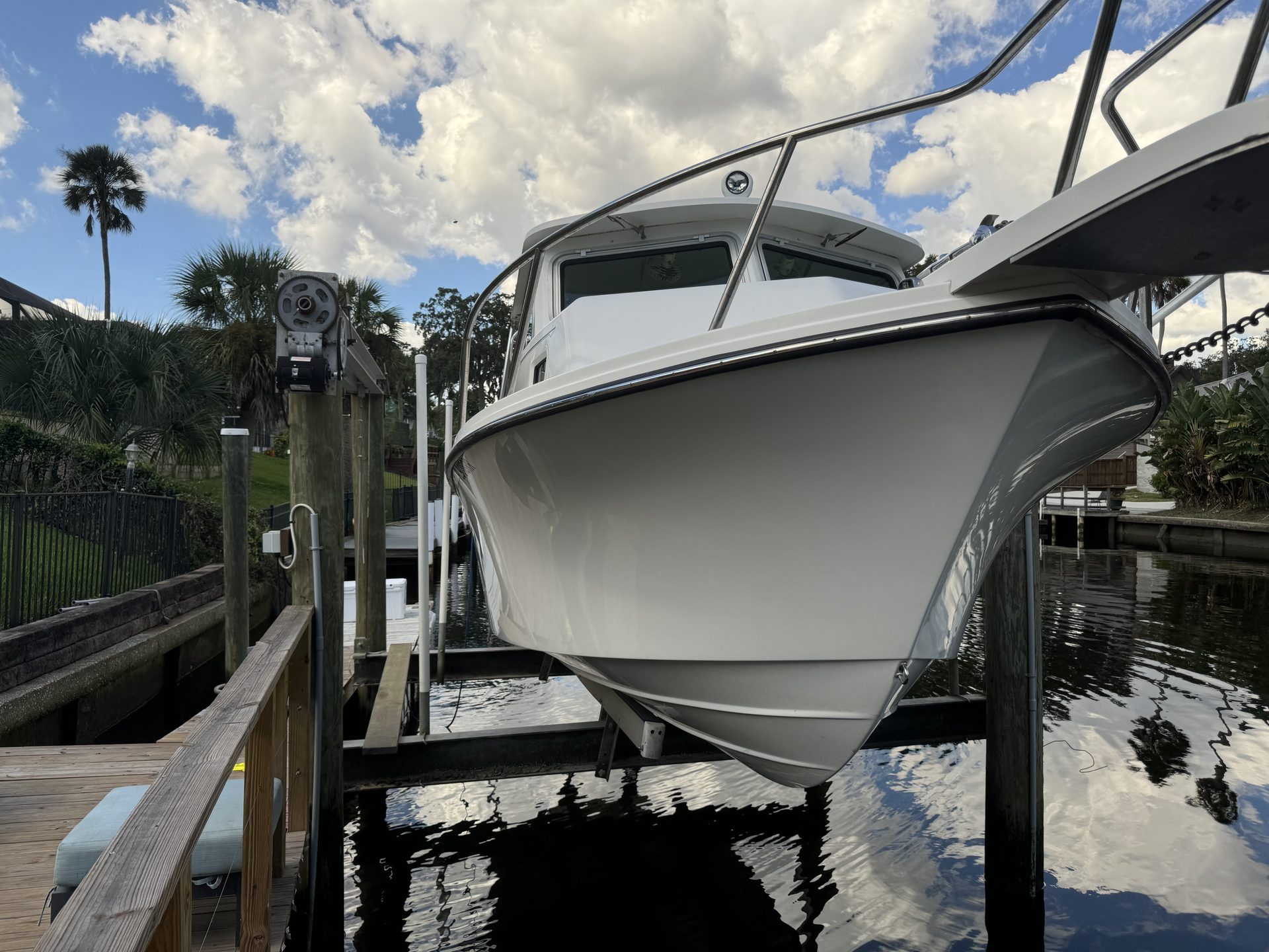 A hardtop boat on a lift, bow toward the camera, palm trees behind