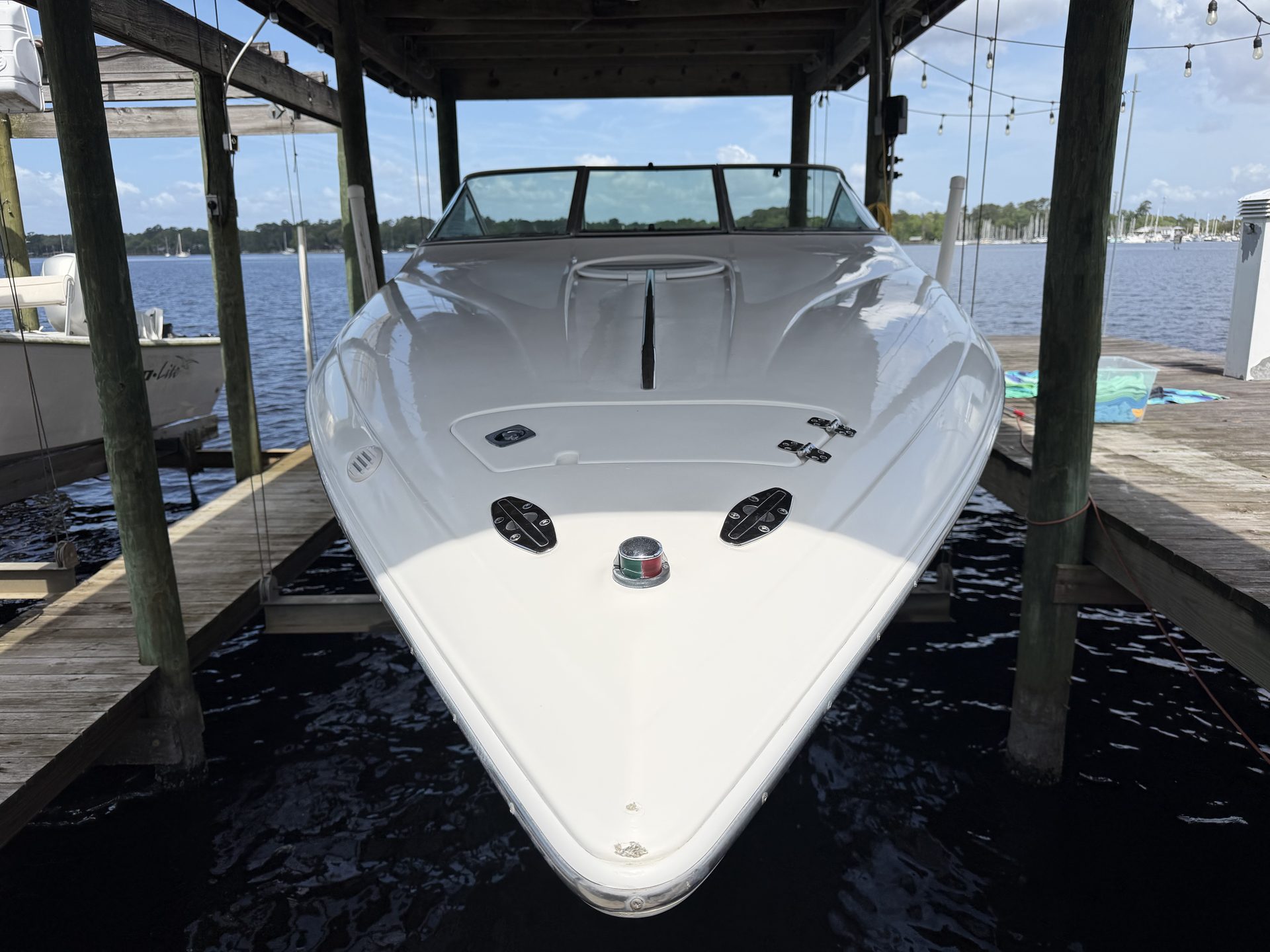 A white cuddy boat on a lift under a boathouse, river behind